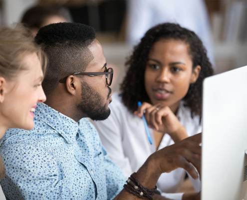 Colleagues working together sitting in front of computer with a more experienced person pointing to the screen.