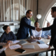 Diverse group of clients thanking professional for help, leader shaking hand on meeting.